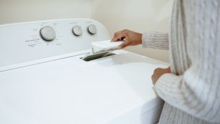 Woman pulling a lint trap out of a white top load dryer.