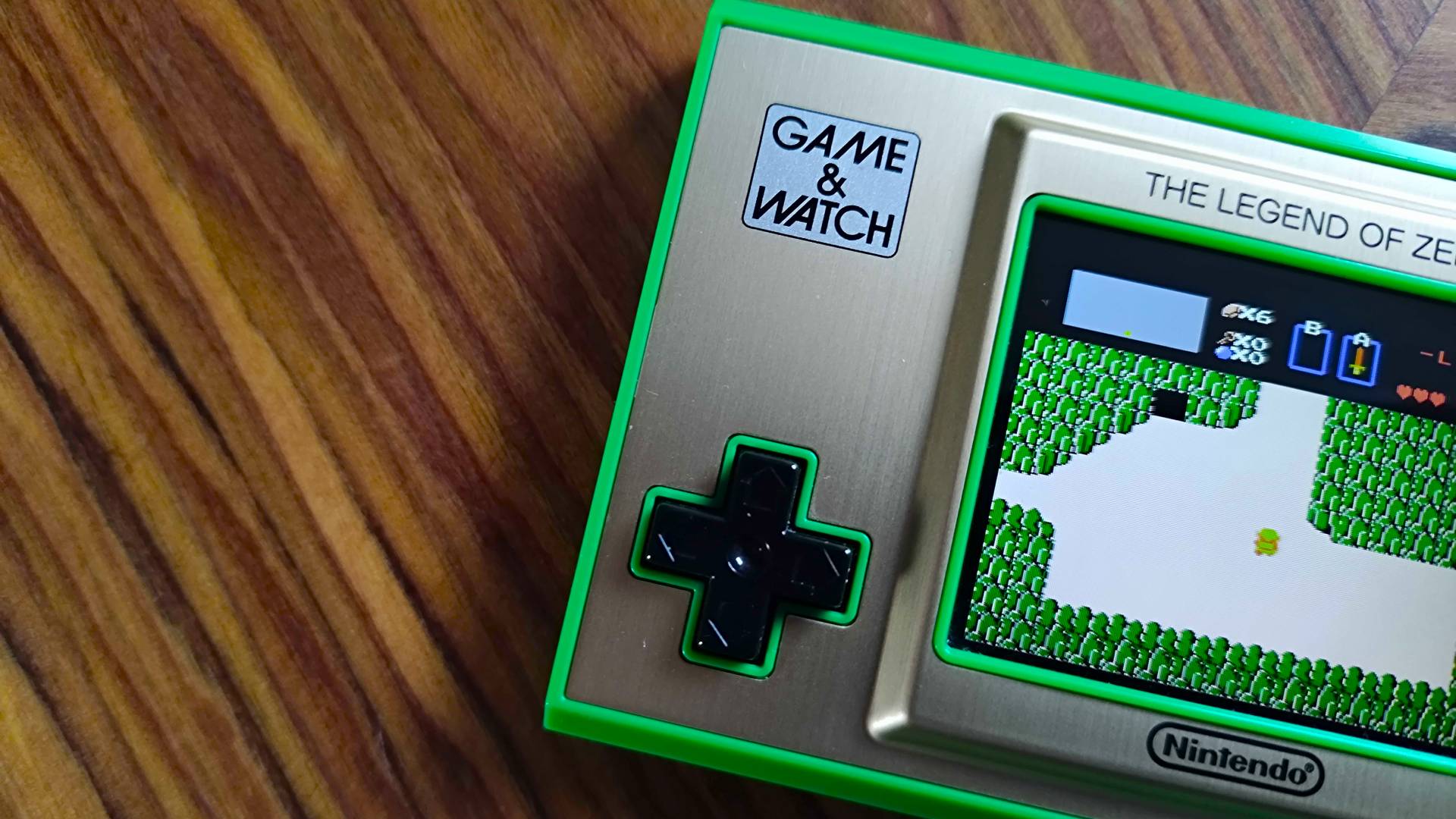 Close up of Zelda Game and Watch d-pad on woodgrain table.