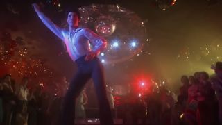 John Travolta dancing in a white suit on a lit up dance floor in Saturday Night Fever