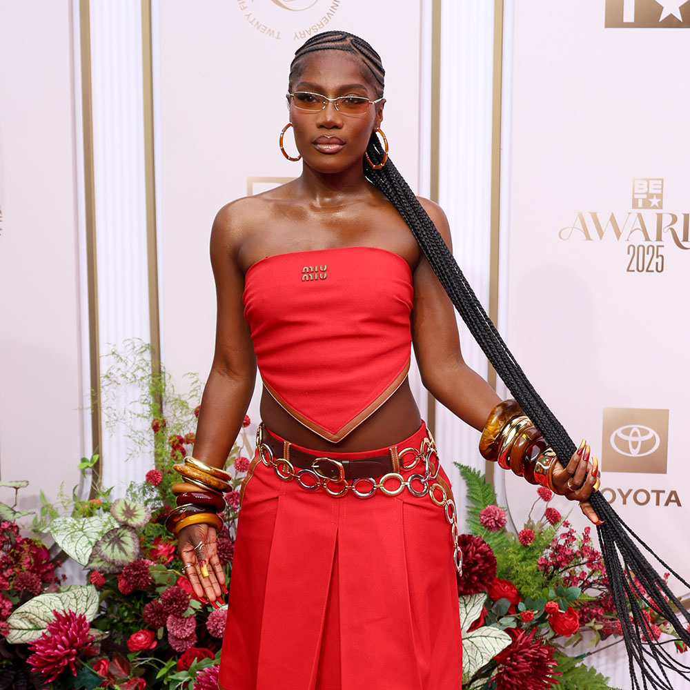 Woman wearing red top and pleated skirt, stacked resin bracelets on each wrist, a metal circular belt, and hoop earrings. 