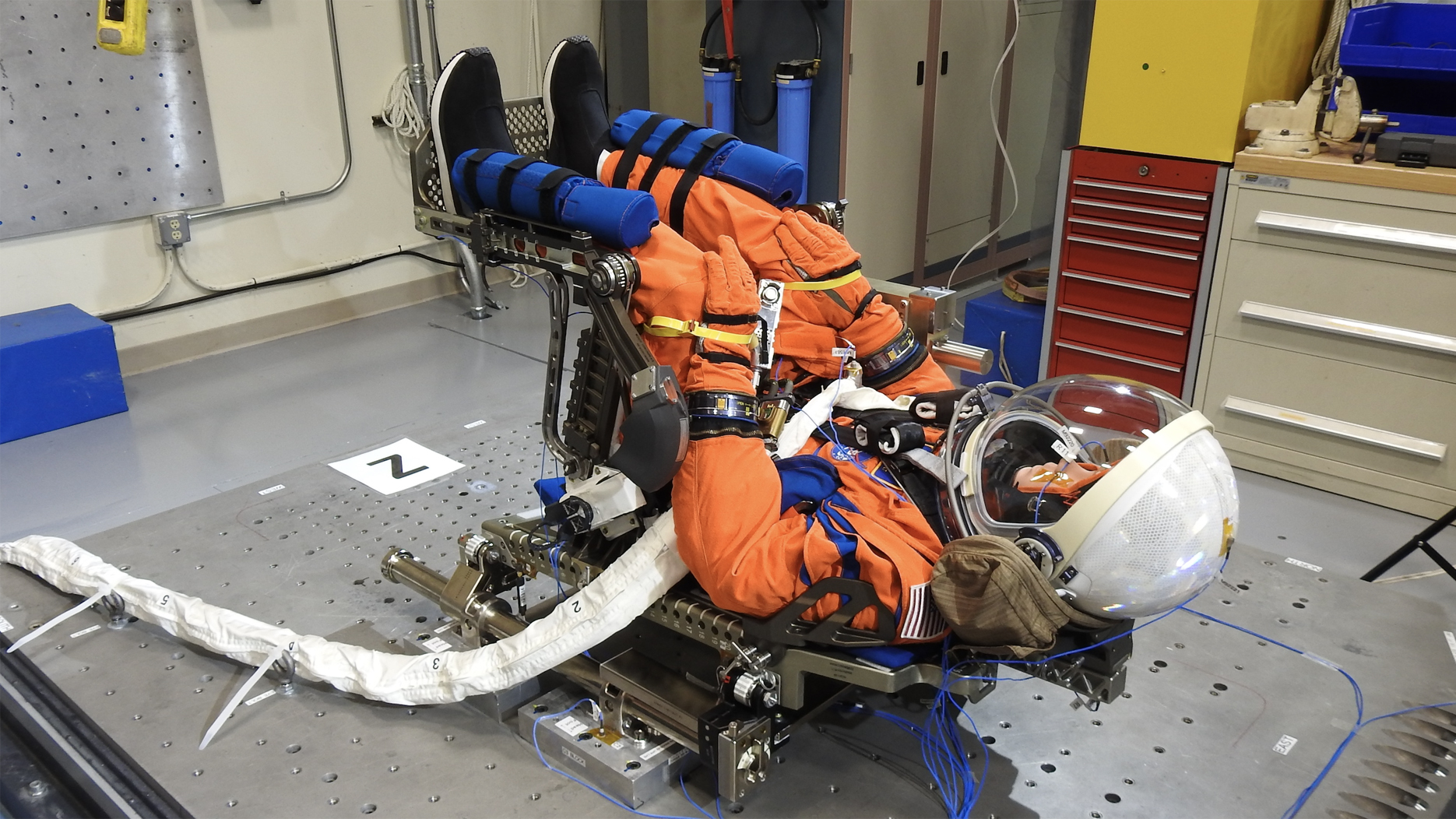 NASA's "Moonikin" mannequin in an orange spacesuits sitting in launch position.