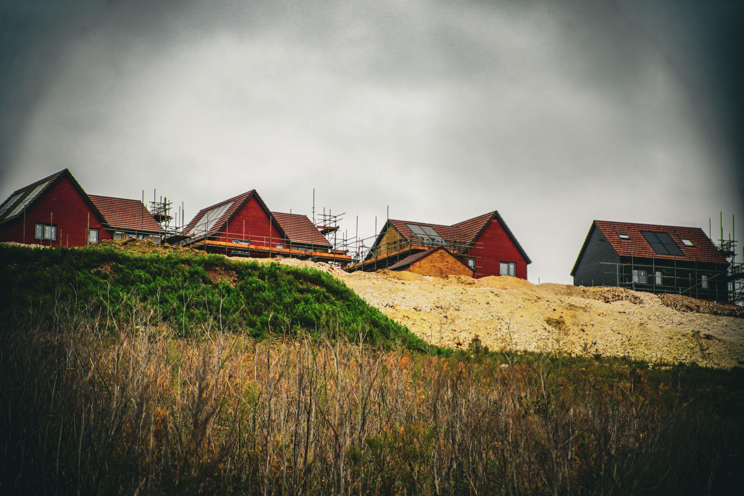 A group of new build houses with scaffolding border a hill of farmland