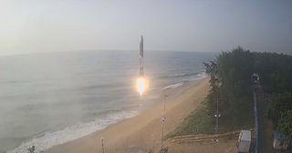 A rocket is seen headed to space in a beachy area.
