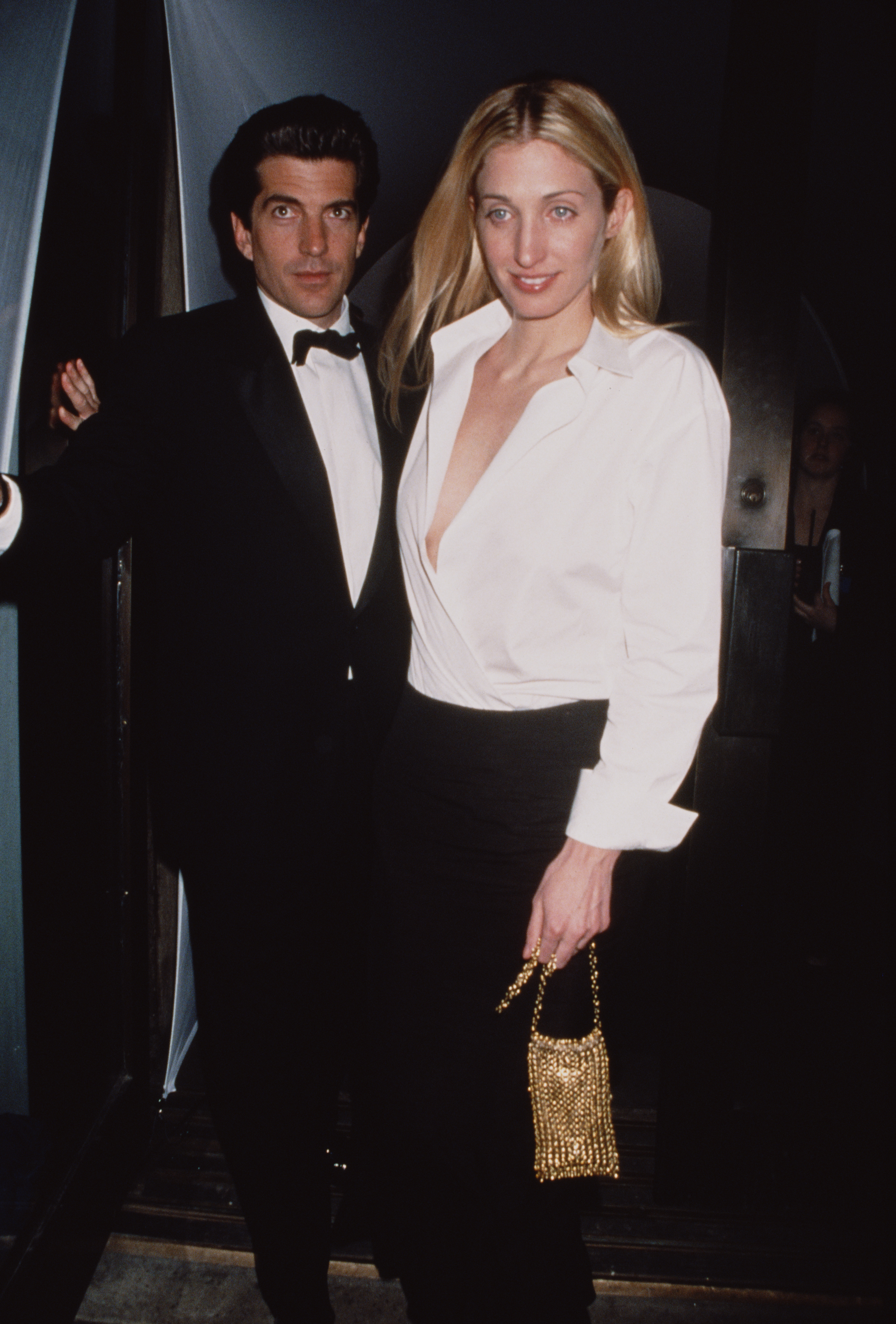 Carolyn Bessette-Kennedy wears a white button down shirt with a black maxi skirt.