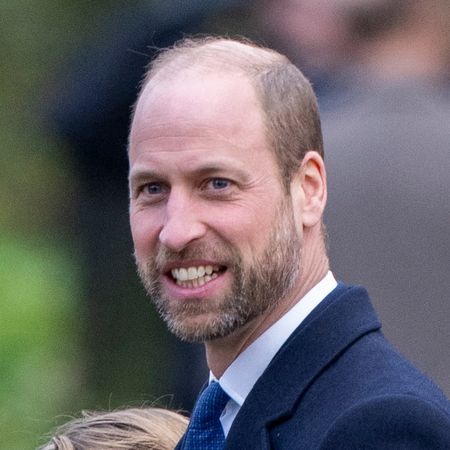 Prince William smiles while wearing a navy suit, he has a beard