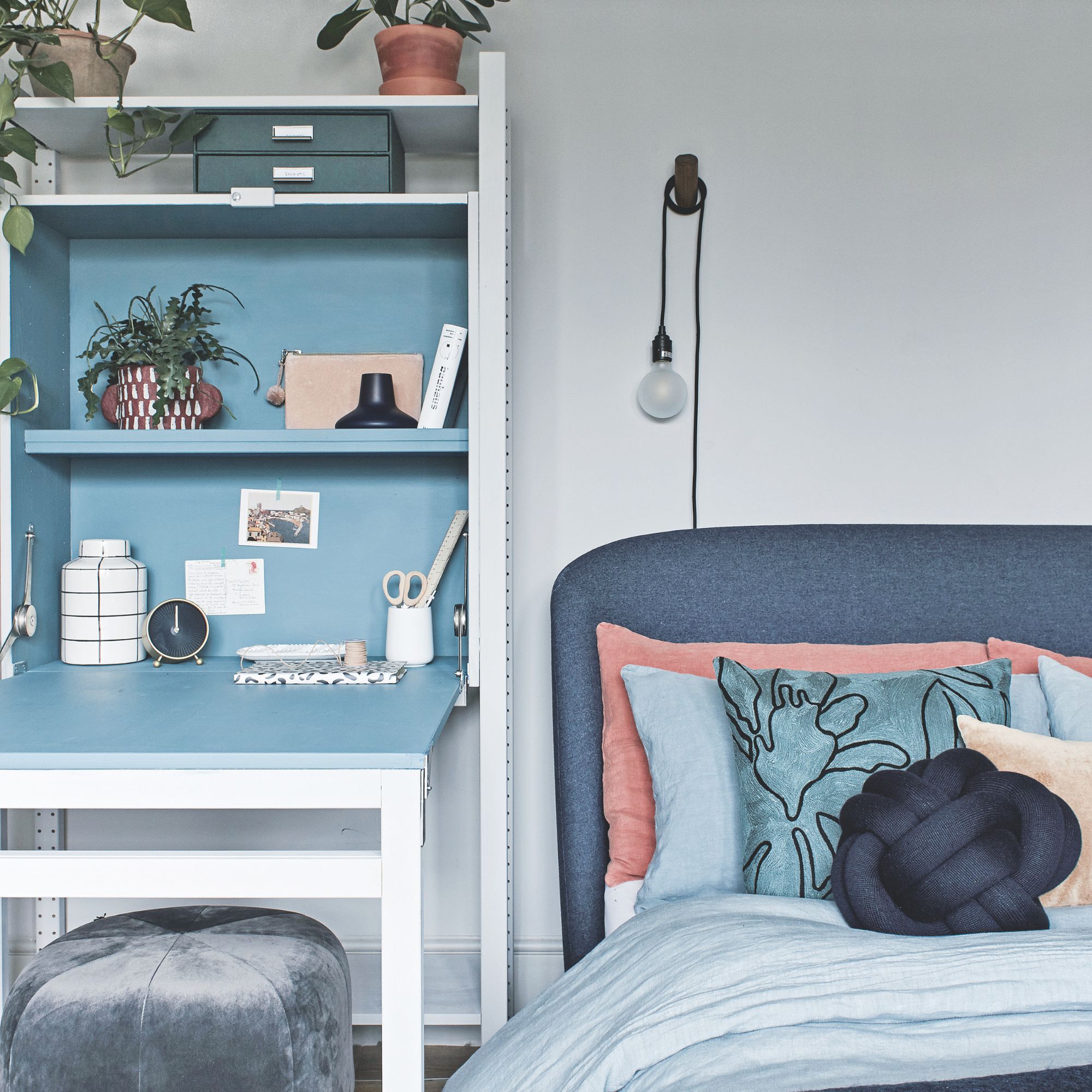 grey painted bedroom with a blue headboard and cushions, with a fold-out work desk next to the bed