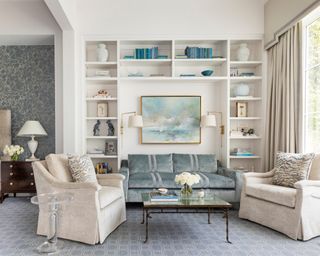 sitting area with blue sofa, neutral armchairs, bookcase and blue artwork