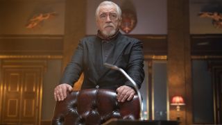 Brian Cox stands behind an imposing leather chair in 007: Road to a Million.