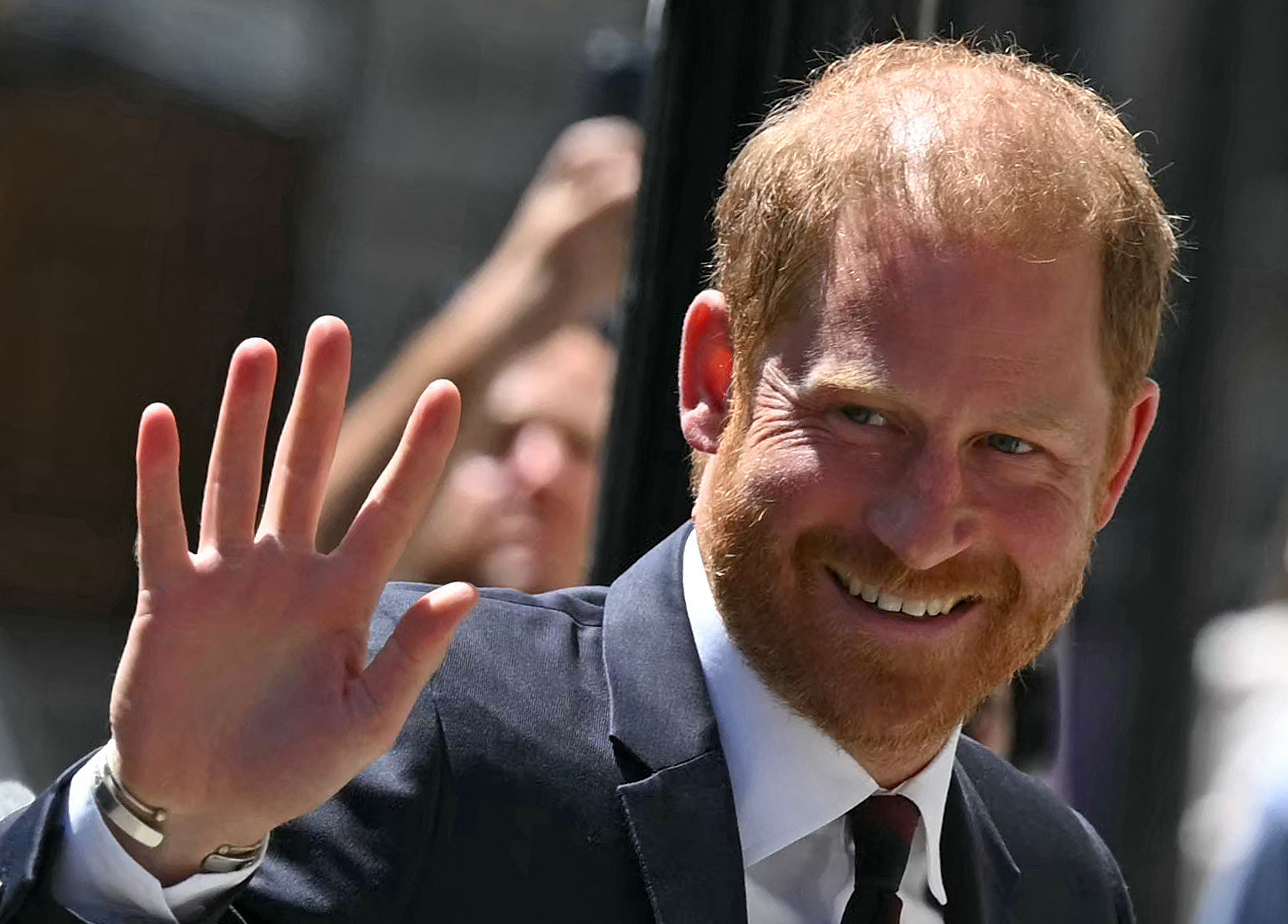 Prince Harry smiling and waving in a suit