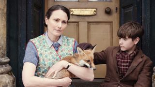 Anna Madeley as Mrs Hall sits on a step holding a fox as Owen Phillips as Christopher Taylor strokes it in the All Creatures Great and Small Christmas Special 2024.