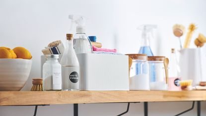 Wooden shelf full of cleaning products, including white vinegar and baking soda