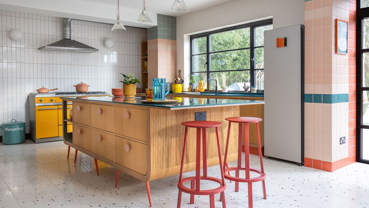 Freestanding wooden island with red bar stools in a colourful kitchen