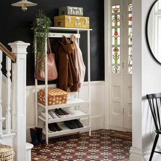 Open shelf with coats and handbags hanging on hooks and shoes on the shelf next to white door with stained glass