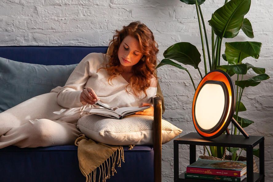 Woman in bed with Lumie Halo SAD lamp on bedside table