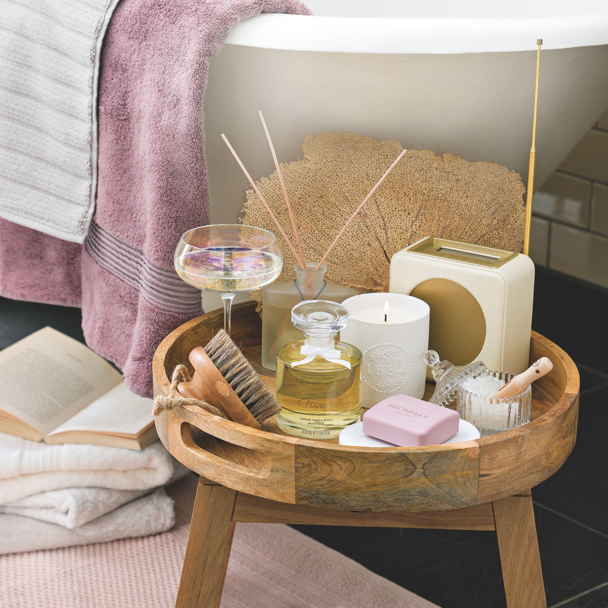 A wooden tray next to the bath with candles and diffusers on it