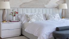 Light, airy bedroom featuring an oversized channel tufted headboard flanked by two nightstands with glossy-based table lamps.