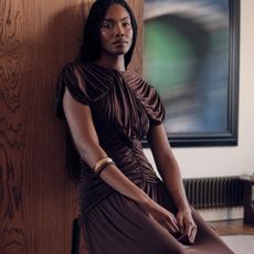 Model wearing a chocolate brown satin Karen Millen dress leaning against a wooden wall