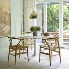 A green-painted dining room with a round dining table and wishbone chairs