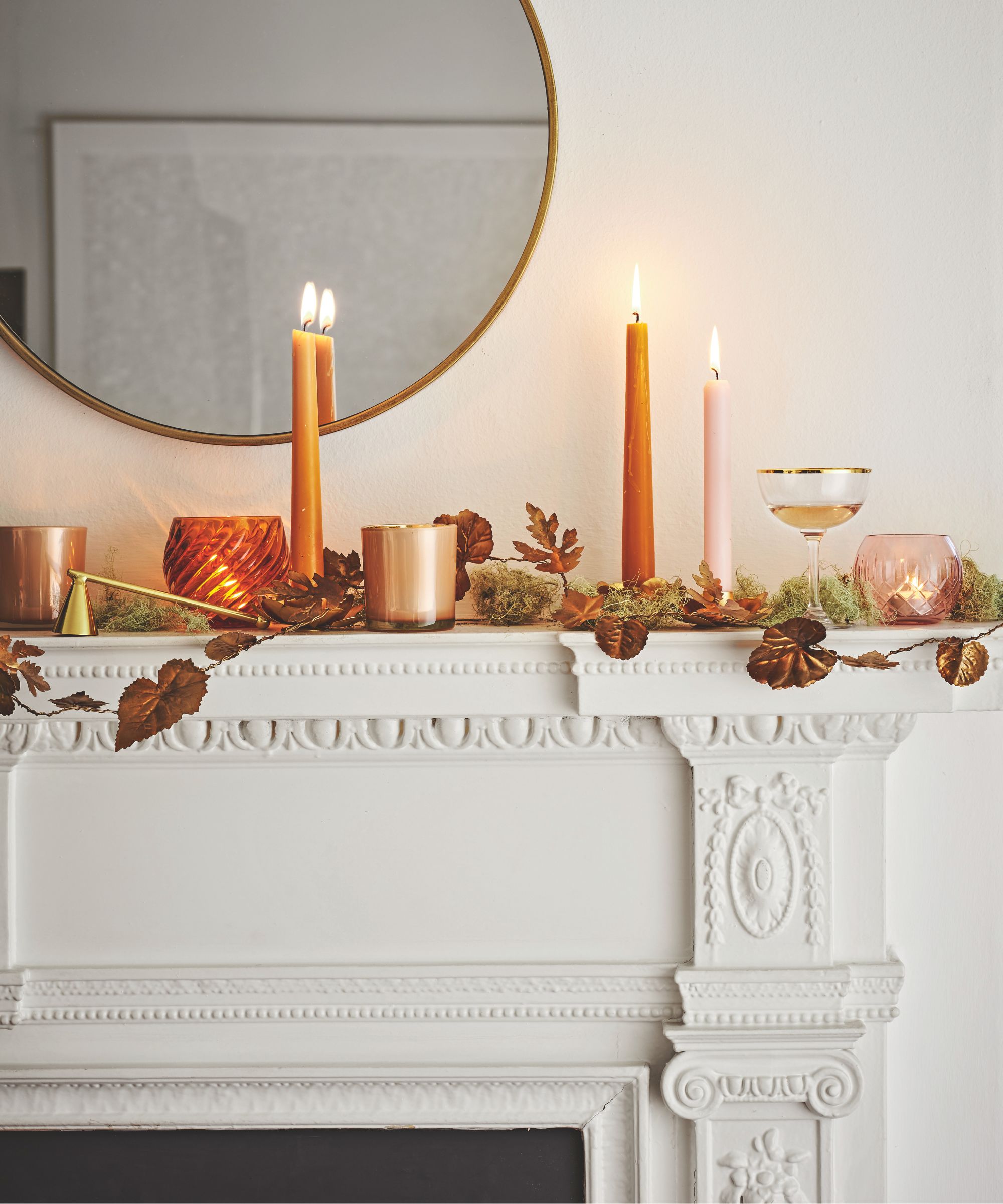A white Autumnal fireplace with leaves, candles, and a circular mirror above