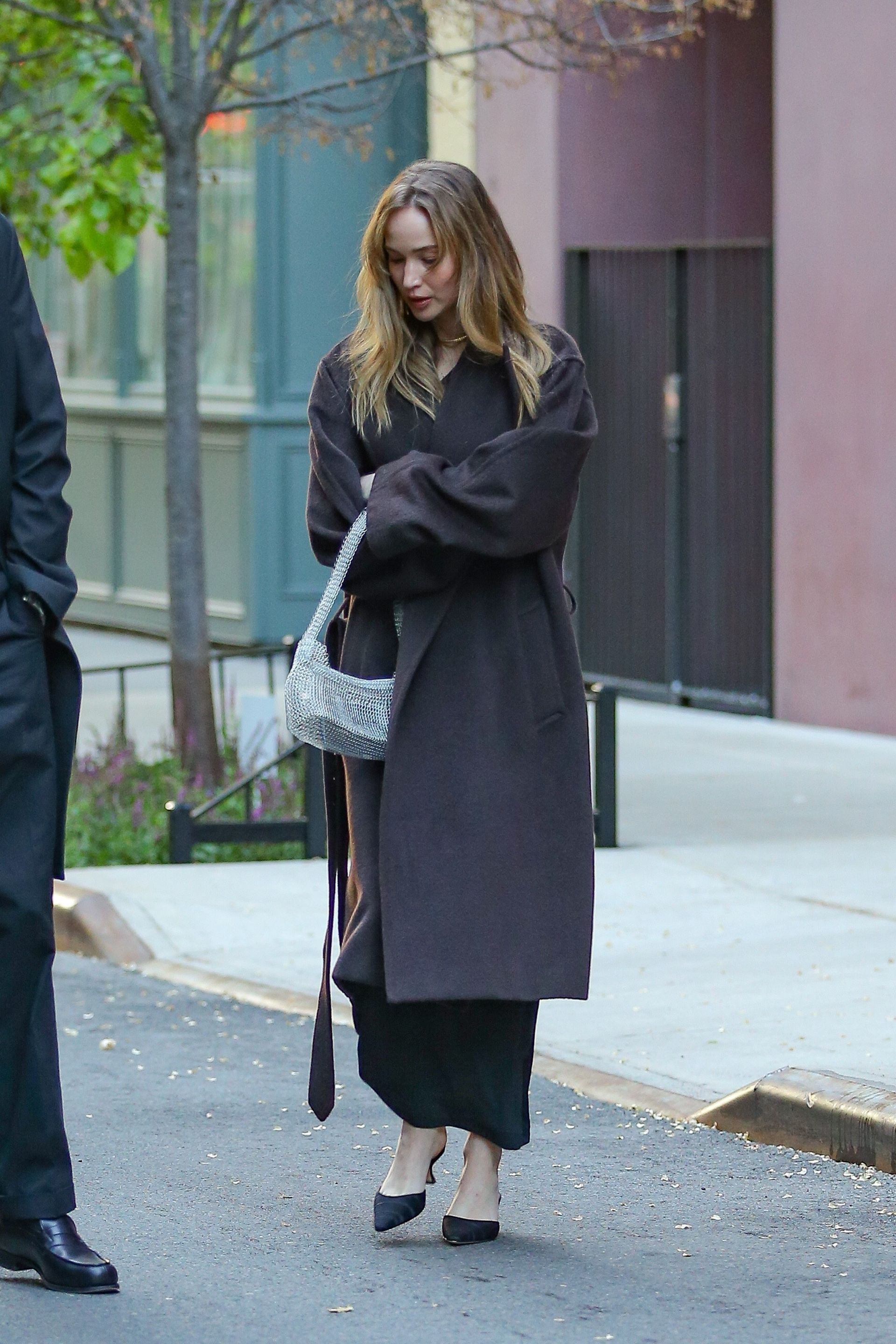 Jennifer Lawrence wears black satin kitten heels with a brown coat and a silver sparkly bag.