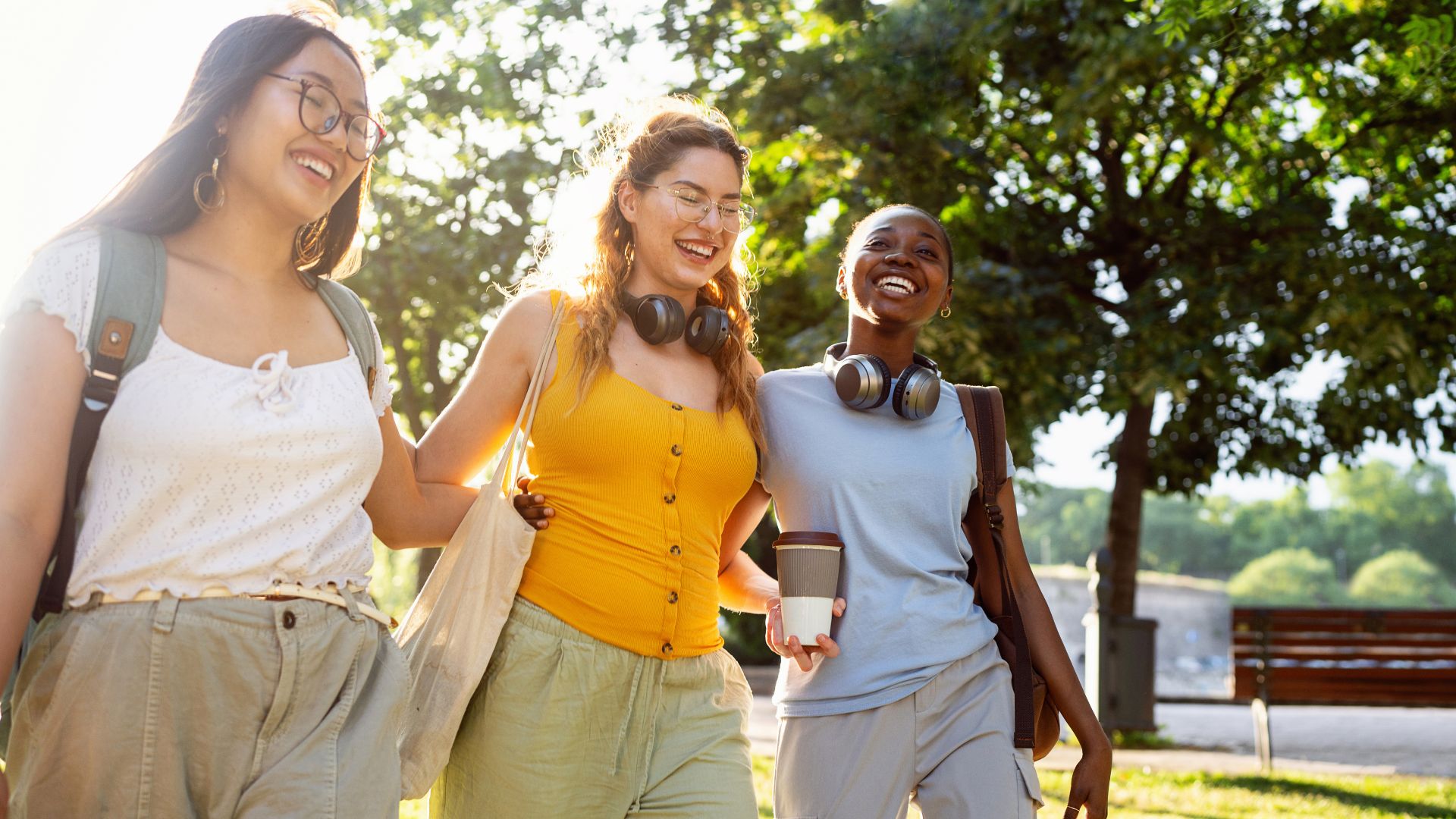 Three female students walk together in a campus park in the sunshine.