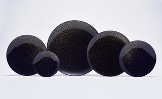 Five black plates of varying size with the same all-over sprinkle style design covering the plate.