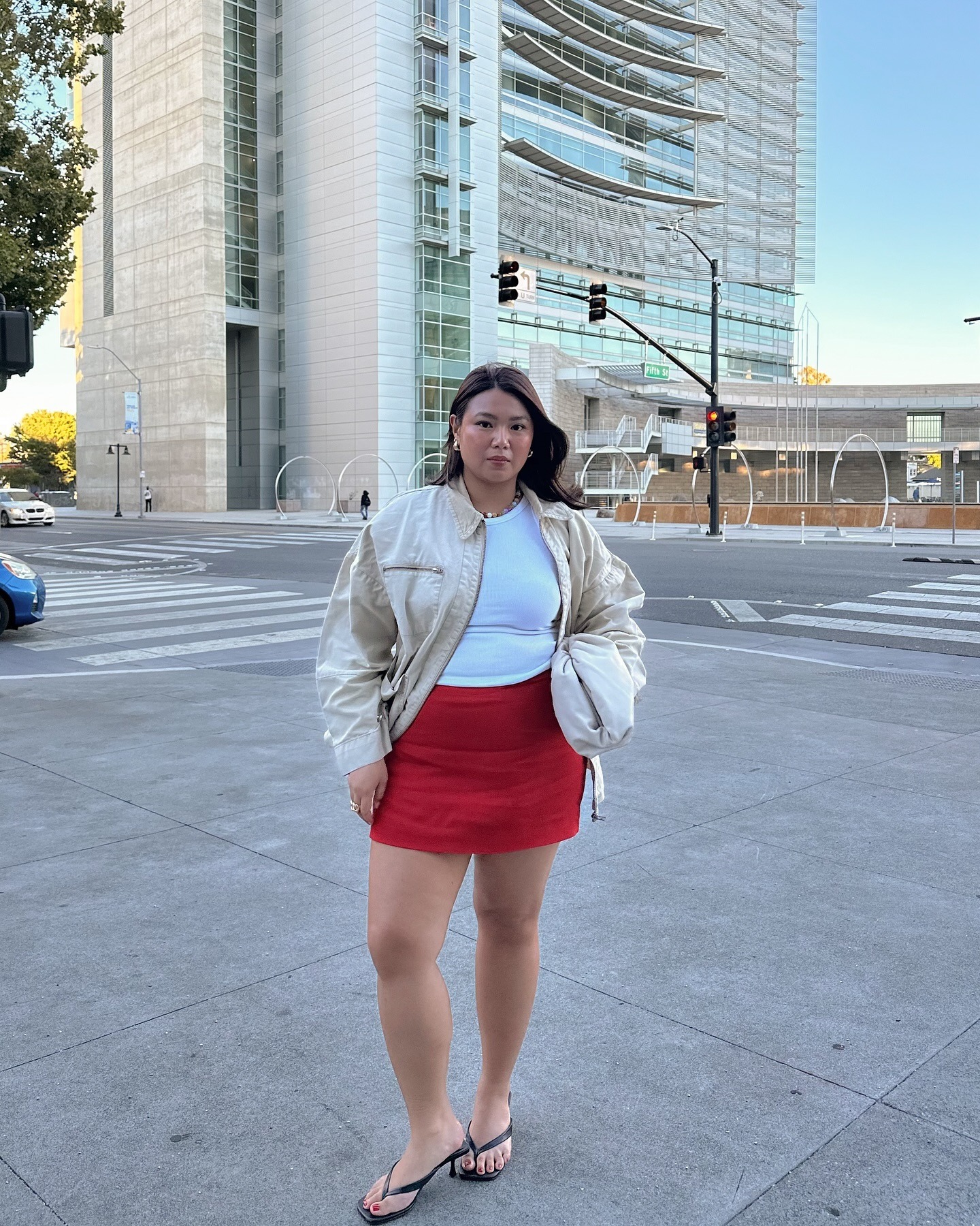 Fashion person Marina Torres wears a red skirt outfit. She pairs it with a bomber, white top, and black thong kitten heels.