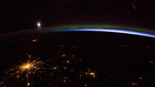 a nighttime photograph from space showing a blue and green aurora borealis and the moon over the lights of Moscow