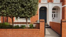 A front garden with a navy blue door and white framing as well as bright orange brick walls with large trees planted in front