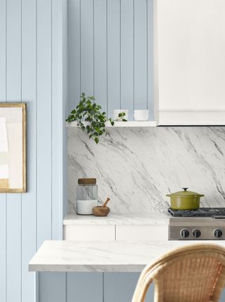 A kitchen with a marble countertop and backsplash and cabinetry painted in a light pastel blue shade
