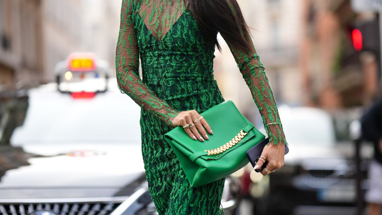 A street style image of a guest at Paris Fashion Week wearing a green lace dress, a green leather clutch bag and winter chrome nails