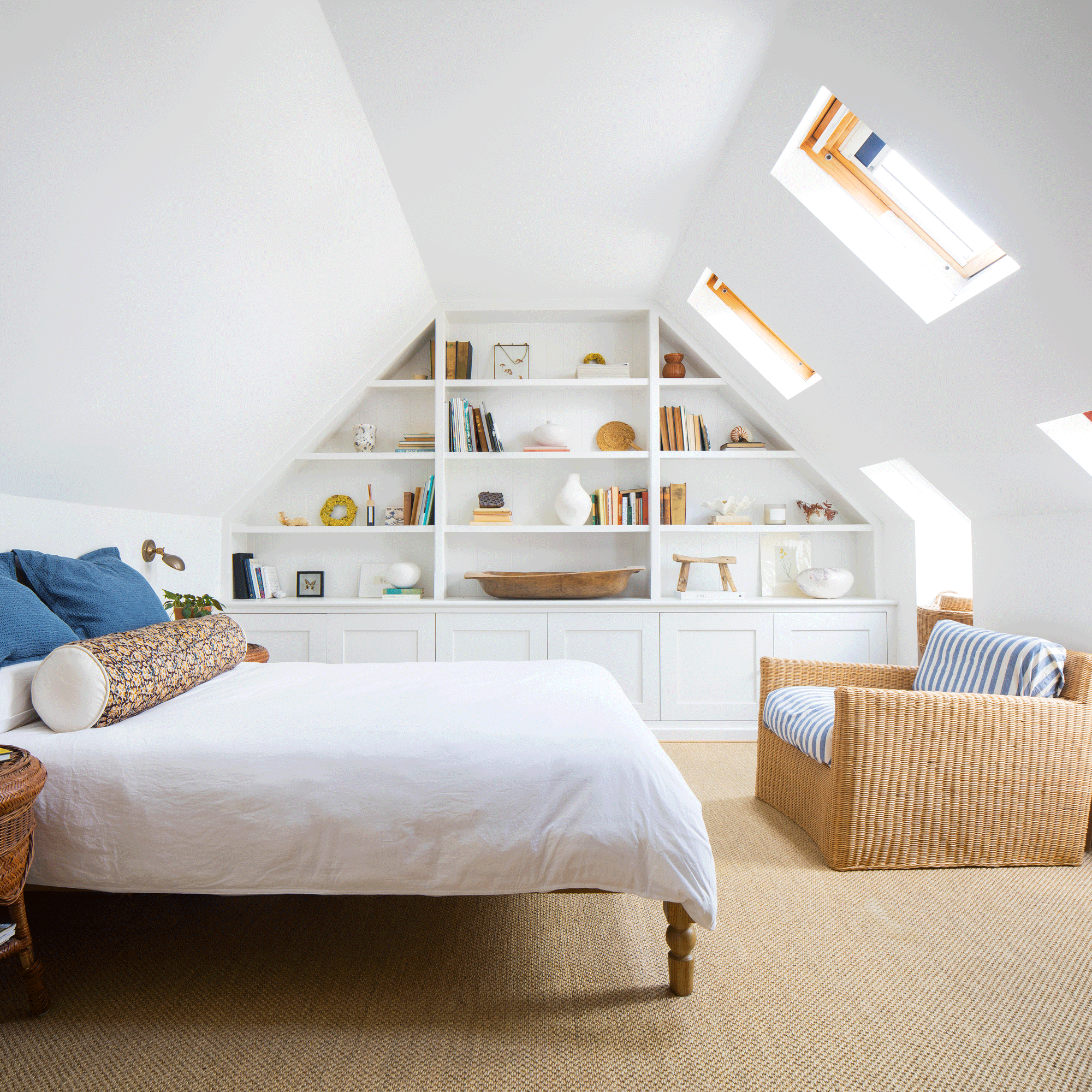 a loft bedroom with a built in feature wall of storage shelving, Velux windows and a bed and armchair