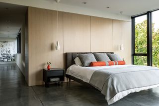 A bedroom with wooden palling, grey bedding and orange throw pillows