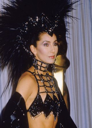 Cher in black sequined outfit with large feathered headpiece
