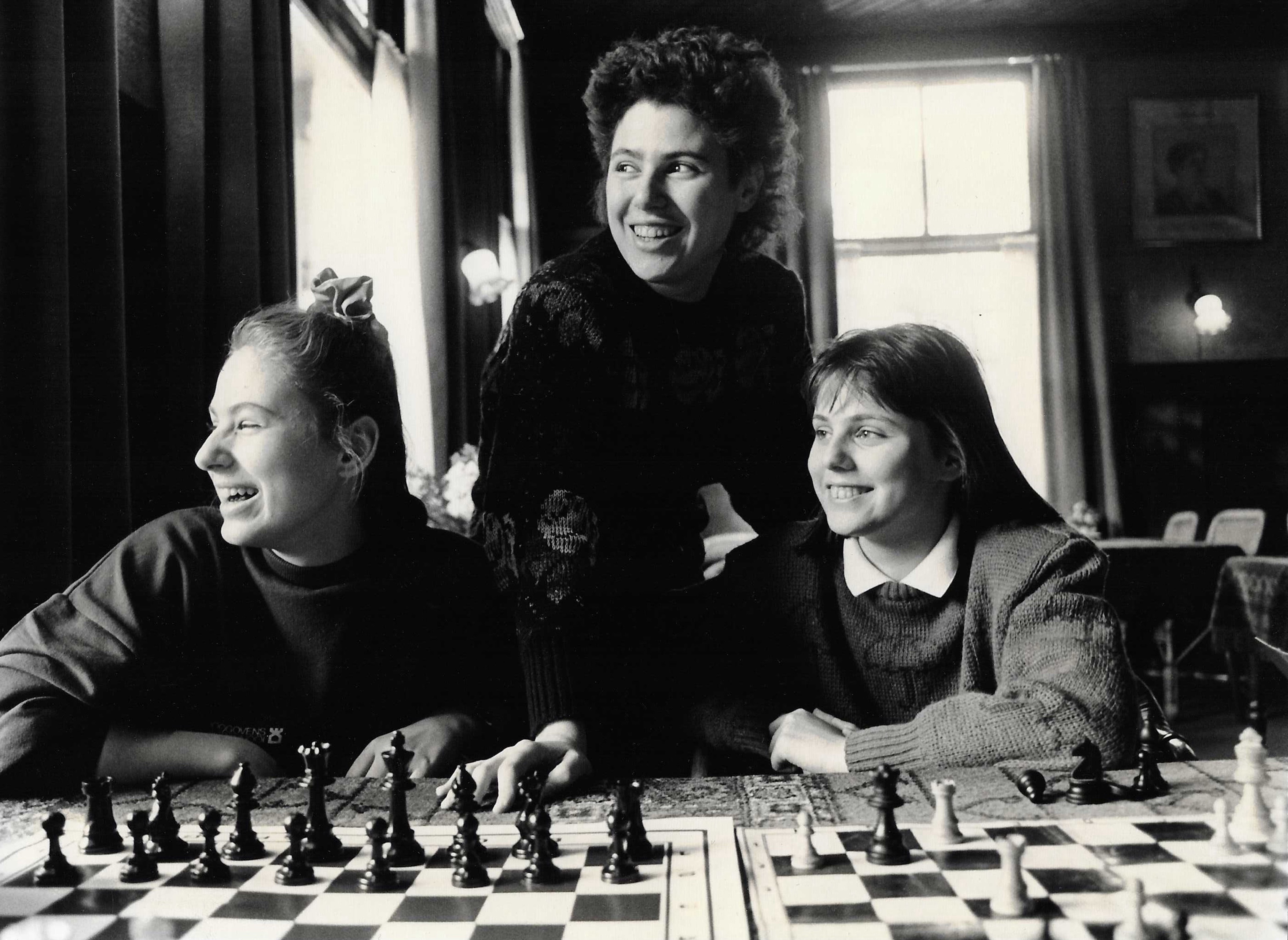 Judit Polg&amp;aacute;r, Susan Polg&amp;aacute;r and Sofia Polg&amp;aacute;r smiling and looking out a window while playing chess in a black and white still from the documentary queen of chess