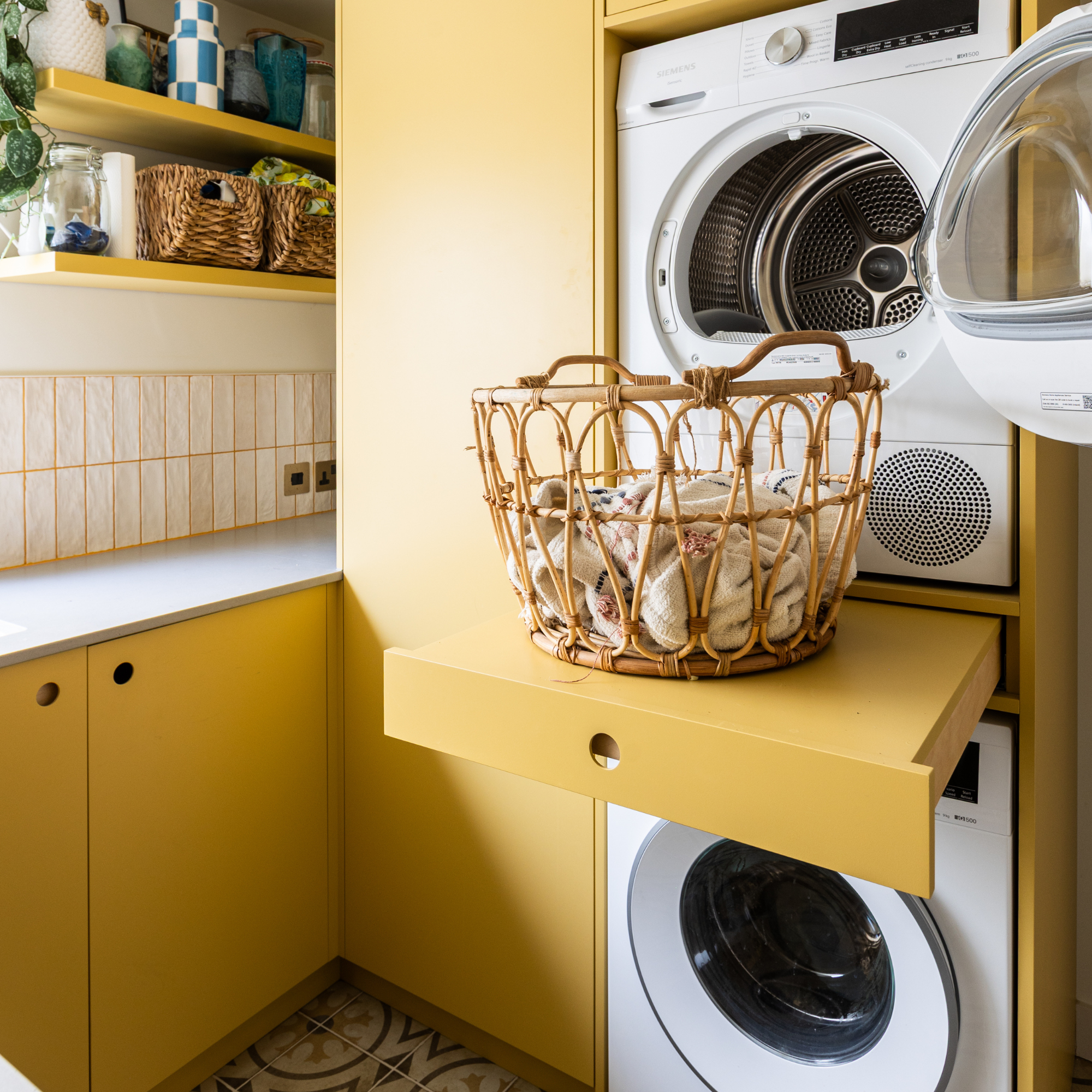 Utility room with yellow cabinets and a stacked washer-dryer, with a pull-out drawer in between them