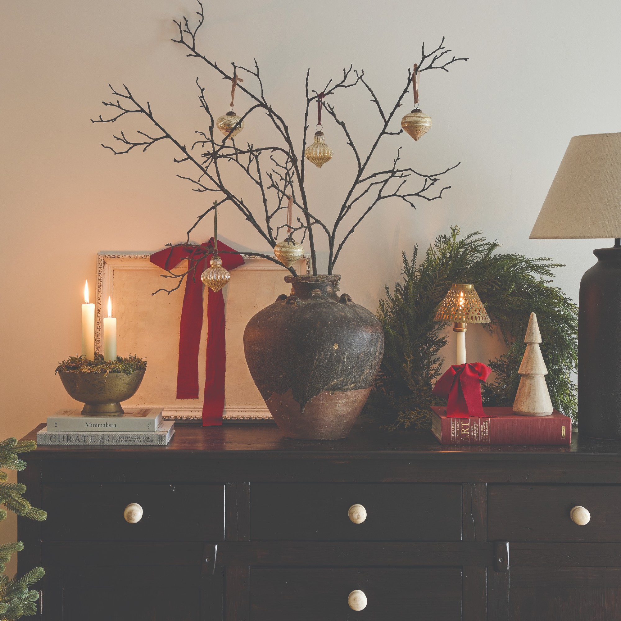 A black sideboard decorated for Christmas with a vase filled with foraged branches decorated with baubles
