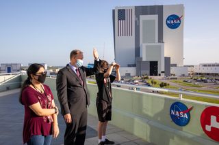 three people stand at NASA's Kennedy Space Center, watching the Mars 2020 mission blast off.