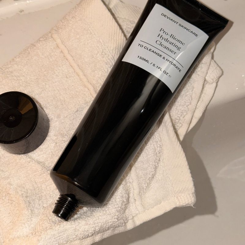 A photo of a cleanser in a black tube on a bathroom sink with a flannel