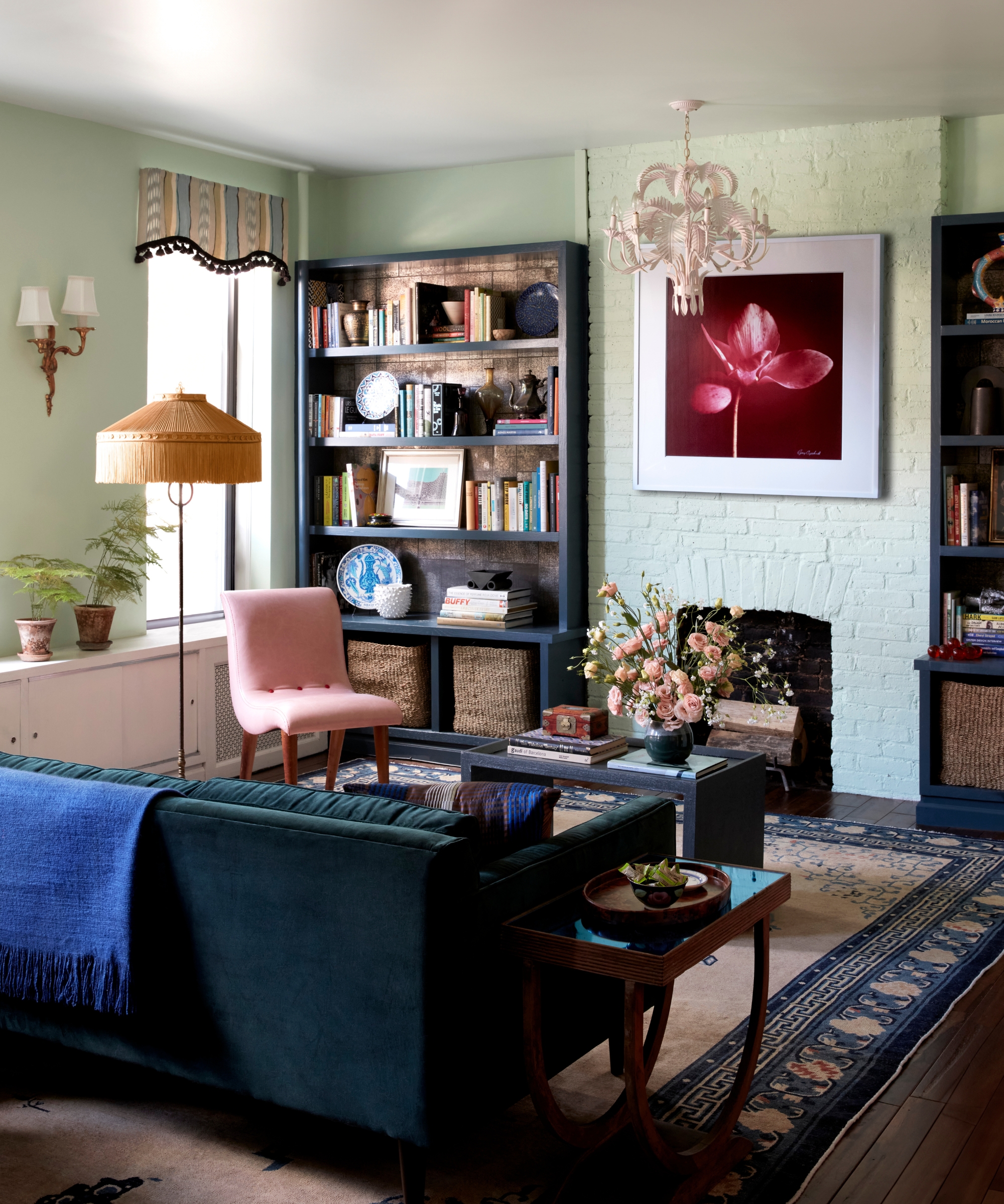 Colorful living room with light green walls, dark blue sofa, frilled lampshades, patterned rug, and a bookshelf full of books and miscellaneous items.
