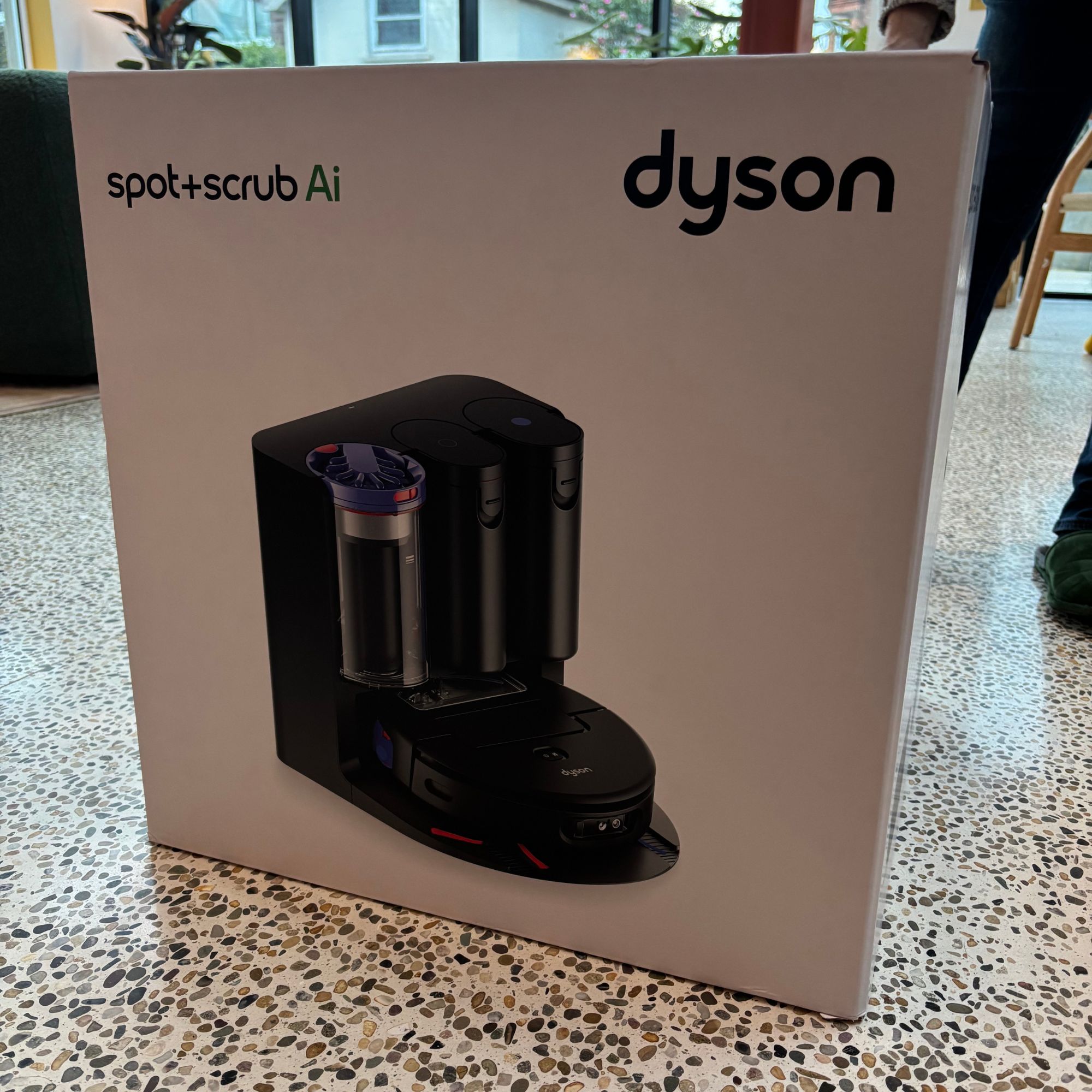 Box of the Dyson Spot+Scrub robot vacuum on speckled concrete flooring
