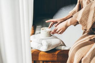 A woman using a body moisturiser next to a full bubble bath.