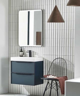 Space-boosting white vertical wall tiles in a tiny bathroom with sink, mirror and black chair.