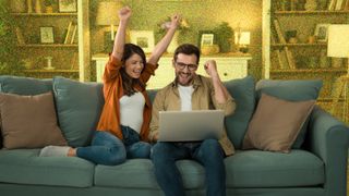 Young couple looking excited whilst sitting on sofa with a laptop.