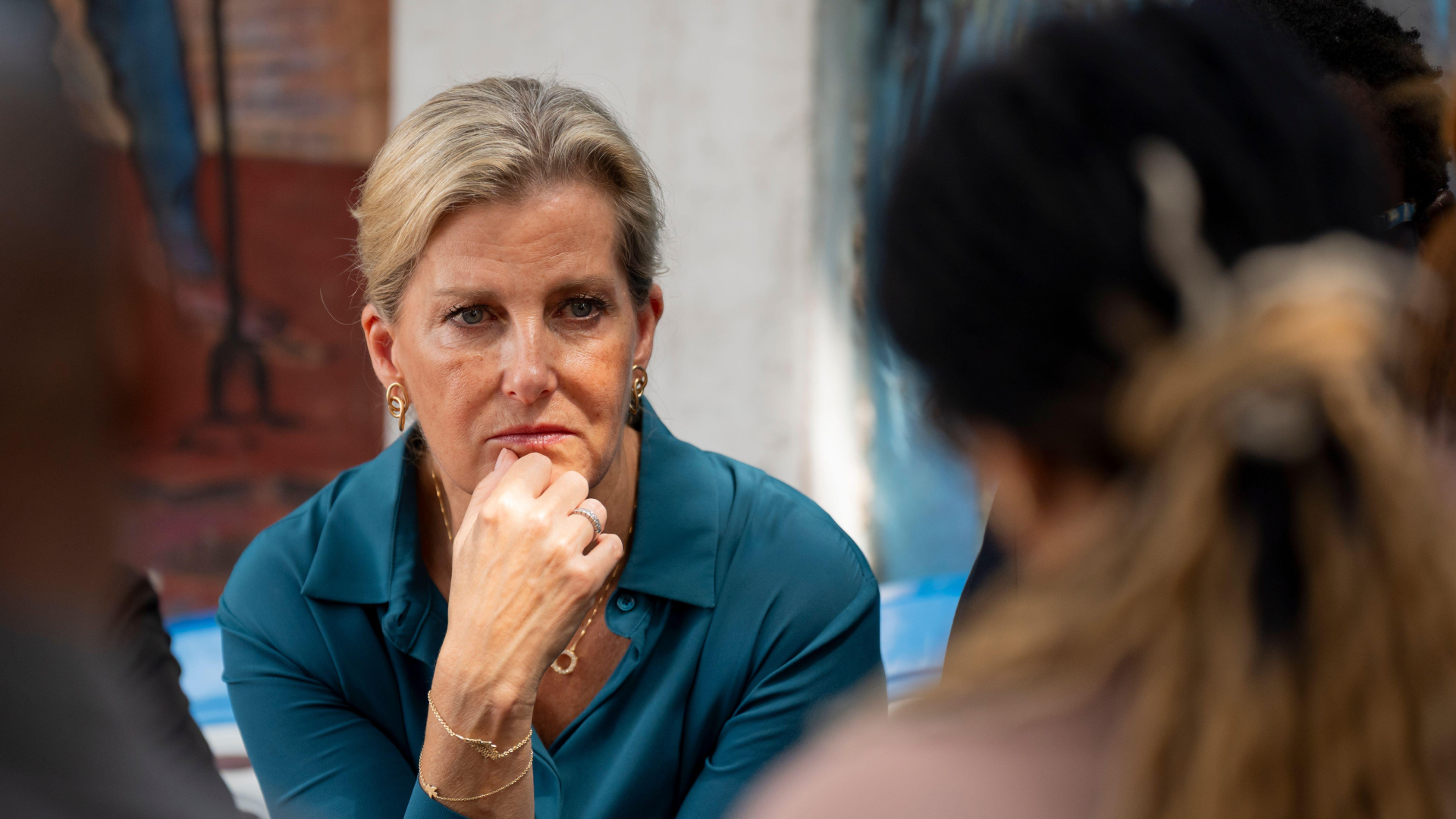 Duchess sophie wearing a teal dress putting her hand on her chin and making a concerned look