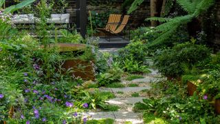 A small garden with a seasting area with two chairs and permeable paving interplanted with ground cover plants