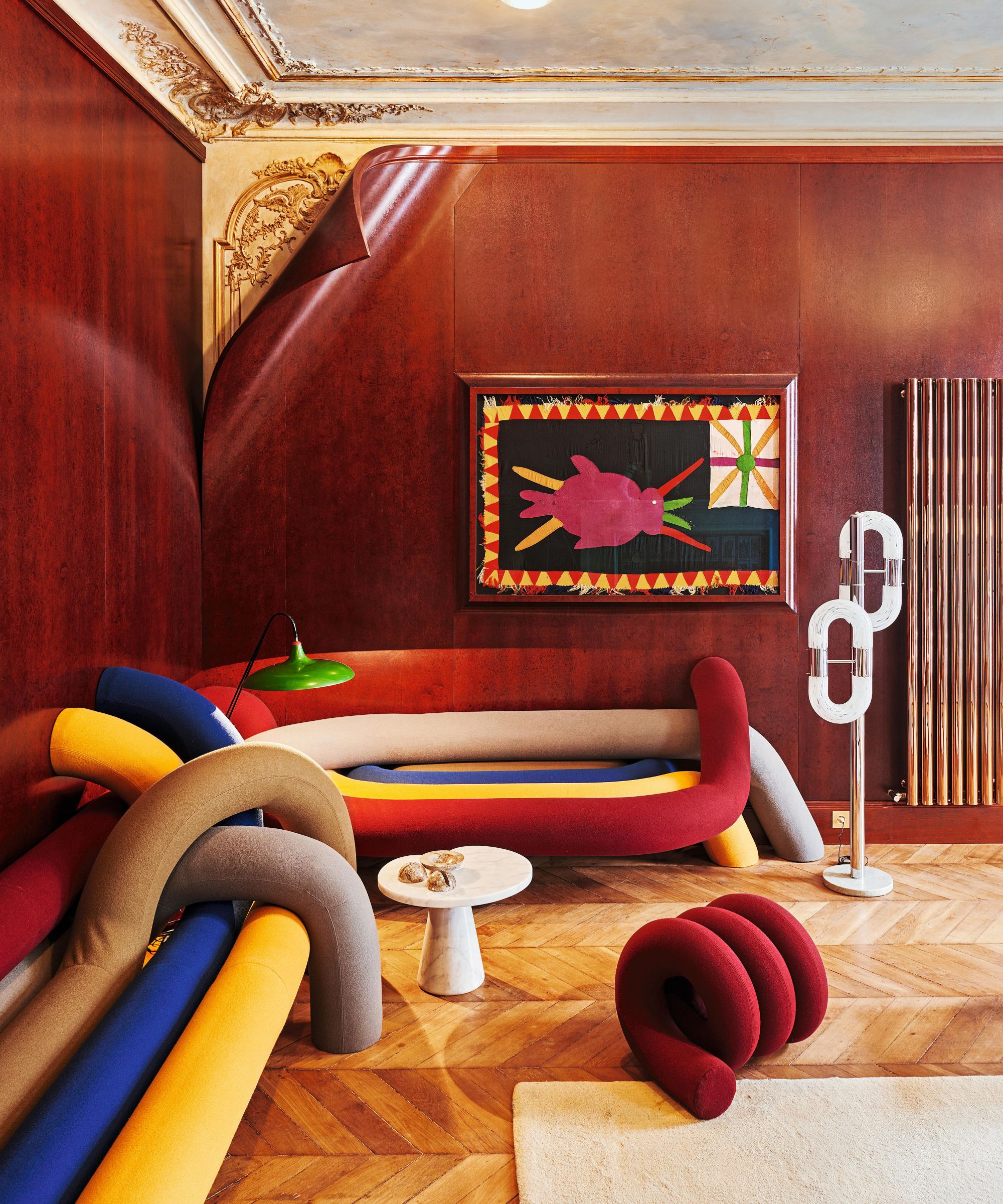 a parisian apartment's eclectic sitting room with a multi-colored sculptural couch and bold artwork