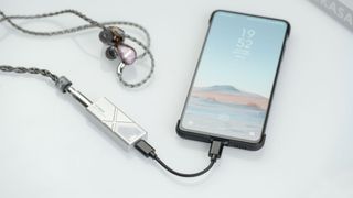 FiiO KA13 DAC attached to a smartphone and wired headphones, on beige background