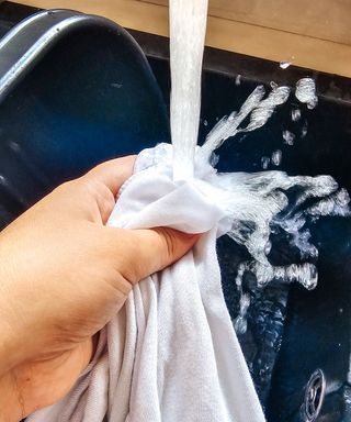 A hand holding a white t-shirt under a faucet with running water