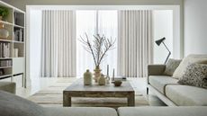 A modern white living room with neutral decor and sliding glass doors with sheer curtains and a heavier neutral curtain.